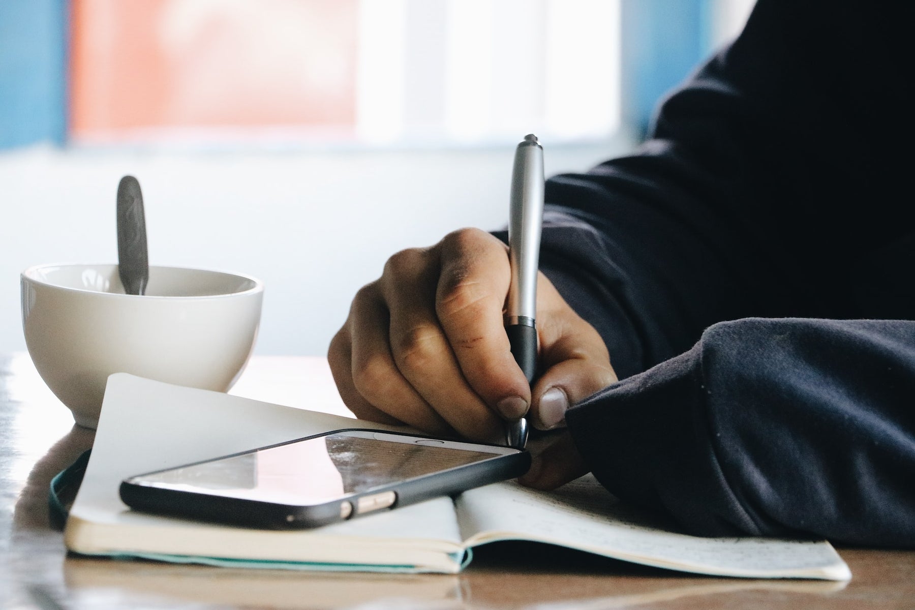 Man writing on notepad while using mobile phone